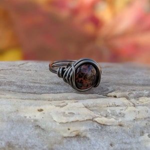 May include: A silver wire wrapped ring with a brown and black speckled stone.