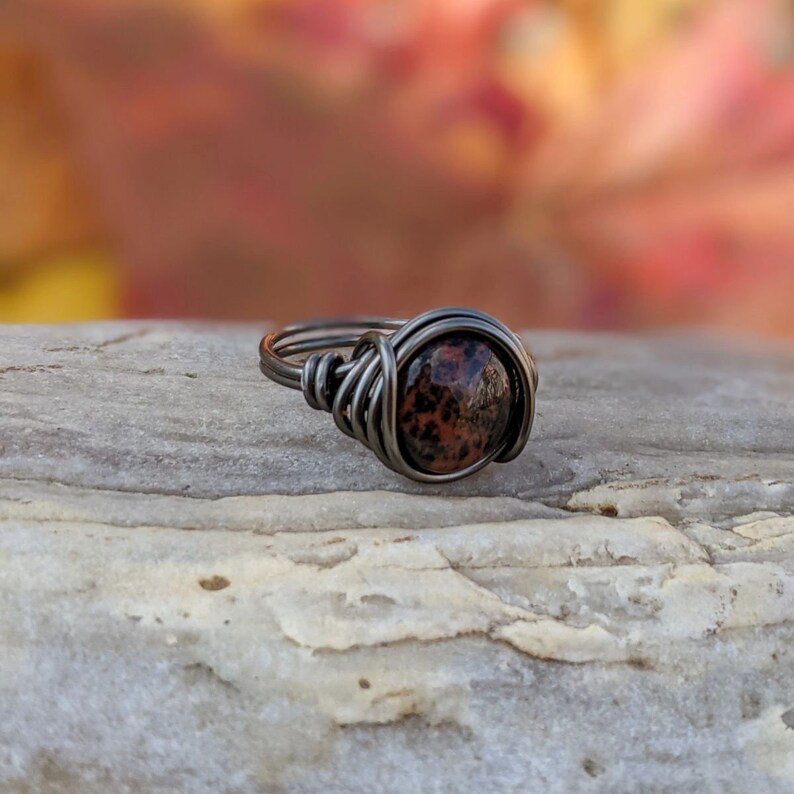 May include: A silver wire wrapped ring with a brown and black speckled stone.