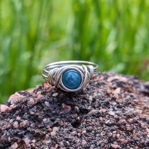Könnte beinhalten: Ein Ring aus Silberdraht mit einem blauen Edelstein in der Mitte.