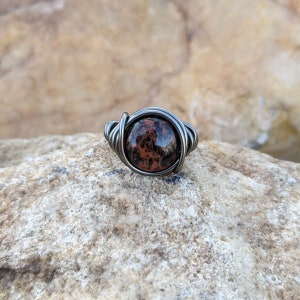 May include: A silver wire wrapped ring with a round, red and black speckled stone.