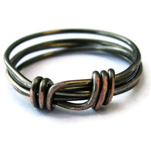 May include: A silver ring with a knot design, made of multiple strands of wire. The knot is accented with a copper wire.