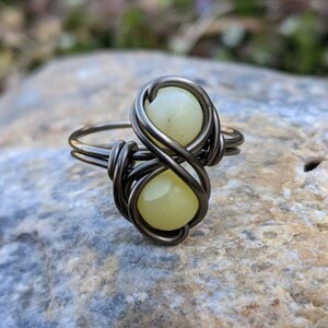 May include: A silver infinity ring with two light yellow gemstones. The ring is made of wire and the gemstones are set in the wire.