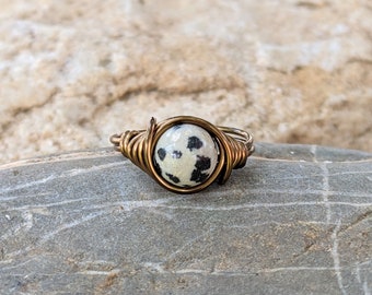May include: A ring with a white and black speckled stone wrapped in brass wire.