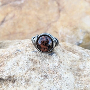 May include: A silver wire wrapped ring with a round, red and black speckled stone.