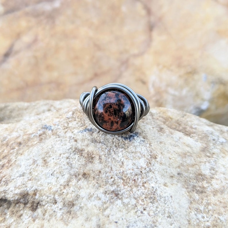 May include: A silver wire wrapped ring with a round, red and black speckled stone.