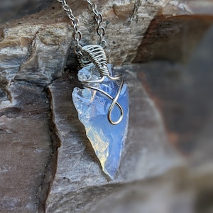 May include: A silver chain necklace with a wire-wrapped, iridescent blue opal arrowhead pendant.