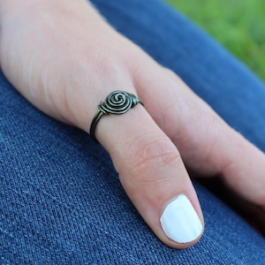 May include: A simple, silver-toned wire ring with a spiral design. The ring is worn on a finger.