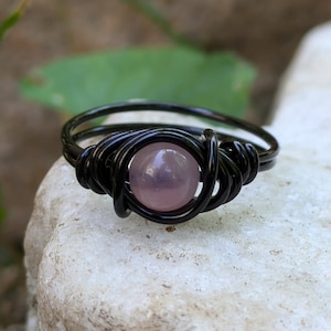 May include: A black wire-wrapped ring with a light pink gemstone.