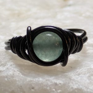 May include: A black wire-wrapped ring with a light blue gemstone.