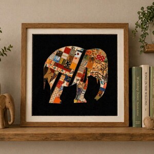 Può includere: Un'opera d'arte incorniciata con la sagoma di un elefante patchwork su sfondo nero. L'elefante è composto da vari motivi di tessuto arancione, rosso e verde. L'opera è esposta su una mensola di legno con oggetti decorativi.