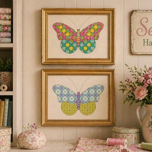 May include: Two framed butterfly art prints with gold frames hang on a wall. The top butterfly has pink, yellow, and green patterns. The bottom butterfly has blue and green patterns. A sign that says "Sew Happy" is above the art.