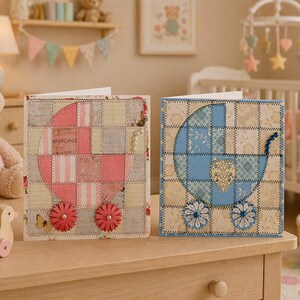 May include: Two handmade baby shower greeting cards. One card features a pink patchwork design of a baby carriage with flower wheels. The other card has a blue patchwork baby carriage design with daisy wheels. Both cards are on a wooden surface.