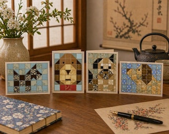 May include: Four greeting cards with patchwork dog designs in various colors, including blue, brown, and tan. The cards are arranged on a wooden surface with a floral notebook, pen, and vase of flowers.