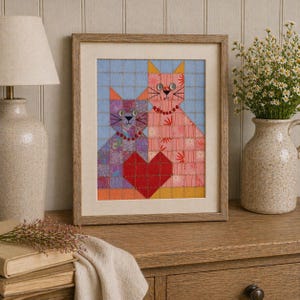 May include: Framed artwork featuring two stylized cats with a red heart. The cats are composed of patchwork fabric in pink, purple, and orange hues, set against a light blue background. The artwork is in a light brown wooden frame.
