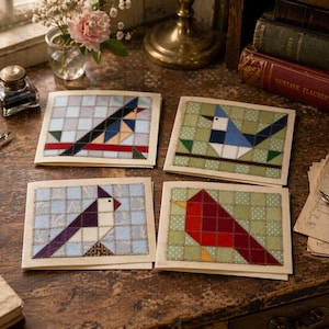 May include: Four handmade greeting cards with bird designs. Each card features a different bird, constructed from fabric patches in various colors, set against a grid background. The birds are in shades of blue, red, and purple.