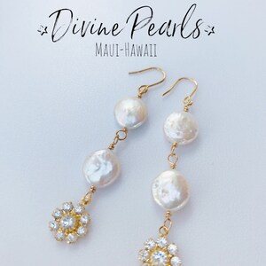 May include: Gold-toned drop earrings featuring three large, white, coin-shaped pearls and a sparkling, flower-shaped cluster of clear crystals. The earrings are suspended from gold-colored ear wires. The text "Divine Pearls" and "MAUI-HAWAII" are in the image.