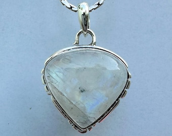 May include: A silver pendant with a large, pearlescent, triangular moonstone. The stone has a subtle play of color. The pendant hangs from a silver chain. The jewelry is set against a light blue background.