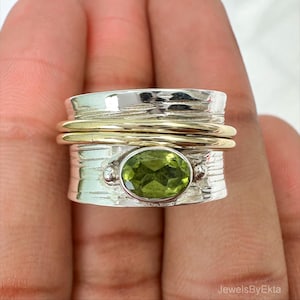 May include: A silver ring with a gold band and a green oval gemstone. The ring has a textured design and a spinning band. The gemstone is a light green colour and is set in a silver bezel.