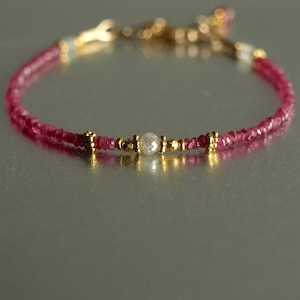May include: A delicate bracelet featuring small, vibrant pink gemstones strung together. The bracelet includes gold-colored accents and a central, faceted, clear gemstone. The jewelry is designed for a refined aesthetic.