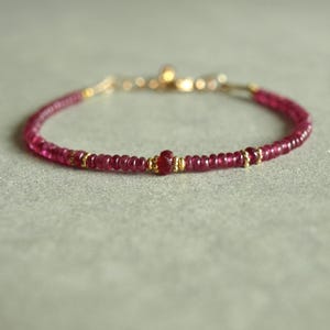 Peut inclure: Un bracelet délicat composé de petites perles rondes rose foncé, entrecoupées d'éléments dorés. Le bracelet est doté d'un fermoir doré et est conçu pour être porté autour du poignet. Les perles sont espacées de manière uniforme, créant un design simple mais élégant.