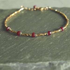 May include: A delicate gold-toned bracelet featuring faceted red gemstones interspersed with smaller gold beads. The bracelet has a simple, elegant design, perfect for everyday wear. The clasp is also gold-toned.