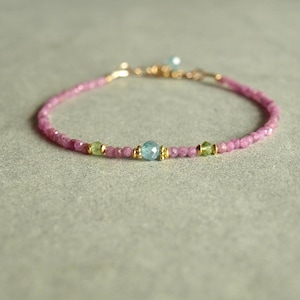 May include: A delicate bracelet made with pink and green gemstone beads and gold accents.