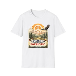 May include: White t-shirt featuring a graphic with a peace sign, mountains, and an eagle. The text "PEACE IS PATRIOTIC" is displayed below the graphic. The design incorporates a sunset and floral elements.