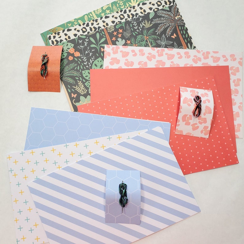 May include: Assortment of patterned scrapbook paper in various colors, including blue, red, white, and green. The paper features different patterns, such as polka dots, stripes, and geometric designs. There are also small pieces of embroidery floss in different colors.