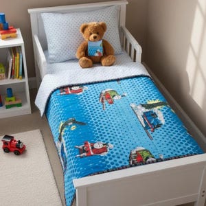 May include: A child's bed with a blue comforter featuring cartoon trains on a blue background with white polka dots. A brown teddy bear sits on the pillow. A red toy train is on the floor.