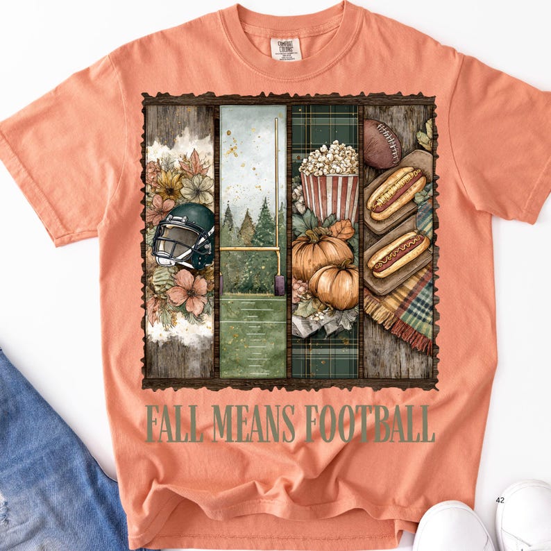 May include: Peach-colored t-shirt with a rectangular graphic featuring football-themed imagery. The graphic includes a football helmet, a football field, pumpkins, popcorn, hot dogs, and the text "FALL MEANS FOOTBALL".