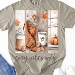 Pode incluir: Camiseta cinza claro com um gr&aacute;fico tem&aacute;tico de outono. O gr&aacute;fico apresenta um caf&eacute; com leite, um su&eacute;ter, uma caneca de caf&eacute; com "hello fall" e uma ab&oacute;bora. O texto "cozy vibes only" est&aacute; abaixo.