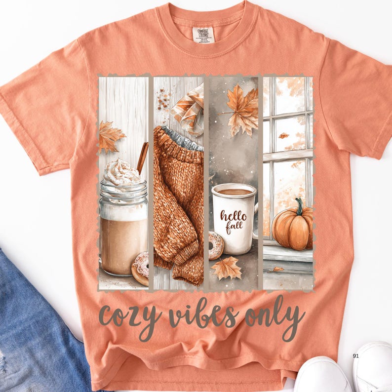 Pode incluir: Camiseta cor de p&ecirc;ssego com um gr&aacute;fico tem&aacute;tico de outono. O gr&aacute;fico inclui um caf&eacute; com leite, um su&eacute;ter, uma caneca de caf&eacute; com "hello fall" e uma ab&oacute;bora. O texto "cozy vibes only" est&aacute; impresso abaixo.