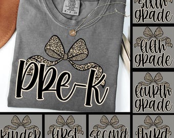May include: Gray Comfort Colors t-shirt with a leopard print bow design and the text "Pre-K". A gold necklace is draped on the shirt. Additional designs for grades Kindergarten through Sixth Grade are also shown.