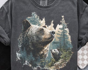 May include: Dark gray sweatshirt featuring a detailed illustration of two bears in a forest setting. The larger bear is in the foreground, with a smaller bear visible in the background. The design incorporates shades of brown, green, and blue.