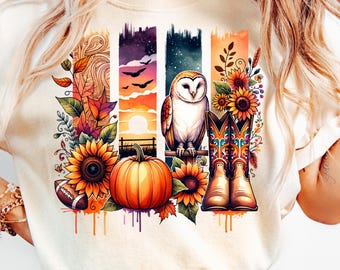 May include: Cream-colored t-shirt featuring a watercolor design with autumn elements. The design includes sunflowers, a pumpkin, an owl, cowboy boots, and a football, set against a backdrop of vertical panels with sunset and night sky scenes.