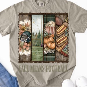 May include: A light gray t-shirt with a graphic design featuring football-themed imagery. The design includes a football helmet, a football field, pumpkins, popcorn, hot dogs, and the text "FALL MEANS FOOTBALL".