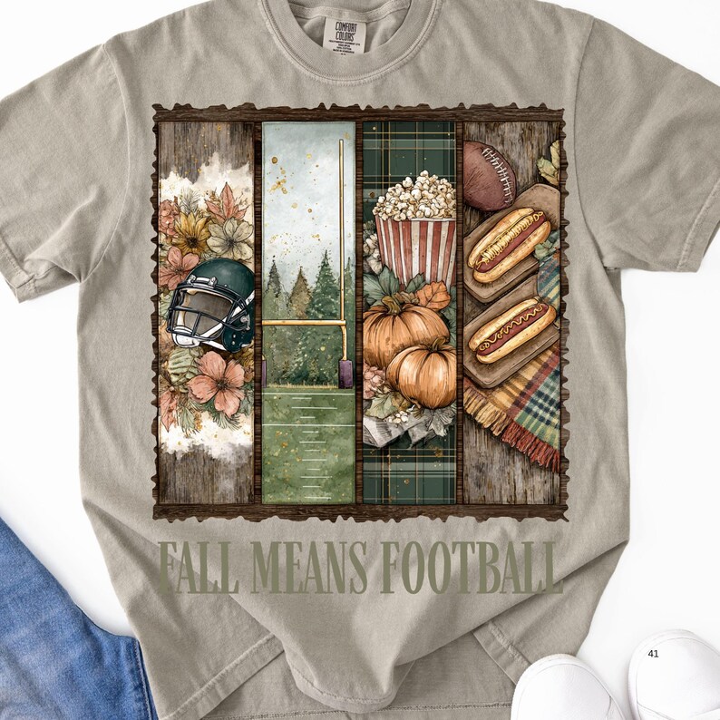 May include: A light gray t-shirt with a graphic design featuring football-themed imagery. The design includes a football helmet, a football field, pumpkins, popcorn, hot dogs, and the text "FALL MEANS FOOTBALL".