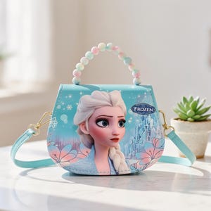 May include: A light blue purse featuring Elsa from the movie Frozen. The purse has a beaded handle and a detachable shoulder strap. The design includes snowflakes, flowers, and a castle. The word "FROZEN" is printed on the purse.