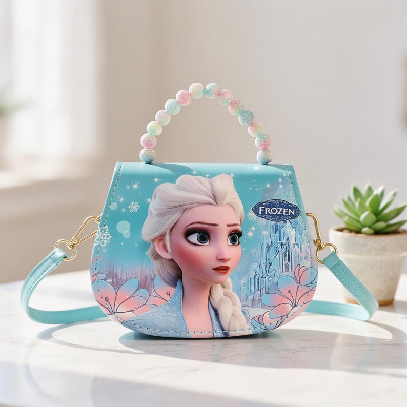 May include: A light blue purse featuring Elsa from the movie Frozen. The purse has a beaded handle and a detachable shoulder strap. The design includes snowflakes, flowers, and a castle. The word "FROZEN" is printed on the purse.
