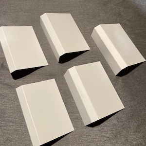 May include: Five light gray, rectangular metal pieces are arranged in a circular pattern on a dark surface. Each piece has a curved top and angled sides, casting shadows.