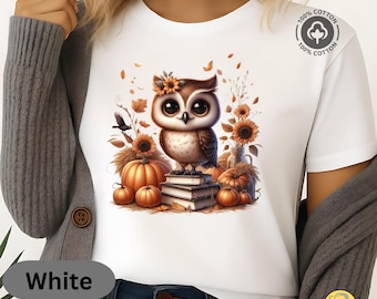 May include: White t-shirt featuring a cartoon owl with large eyes, perched on books, surrounded by pumpkins, sunflowers, and autumn leaves. The shirt has a 100% cotton label and the word "White" is printed on the bottom left.