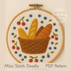 May include: Embroidered hoop art featuring a woven basket filled with bread, surrounded by cherries and blueberries. The design is on a white background with the text "Mini Stitch Doodle" and "PDF Pattern". The hoop is held by a brass-colored clasp.
