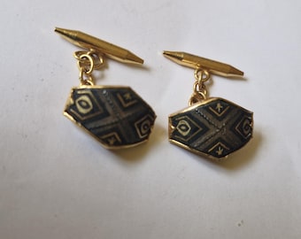 May include: A pair of gold-toned cufflinks with a geometric design. Each cufflink features a dark gray, hexagonal face with a repeating pattern of squares and lines, framed by a gold border. The cufflinks have a classic T-bar closure.
