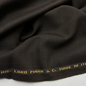 May include: Close-up of a dark brown fabric with subtle folds. The fabric has a smooth texture and appears to be high-quality. The edge of the fabric displays the text "INC. LORO PIANA & C. MADE IN ITA" in gold lettering.
