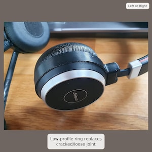 Può includere: Cuffie Jabra nere con un anello argentato. Il logo Jabra è sull'auricolare. Il testo "Left or Right" è in alto a destra. Il testo "Low-profile ring replaces cracked/loose joint" è in basso.