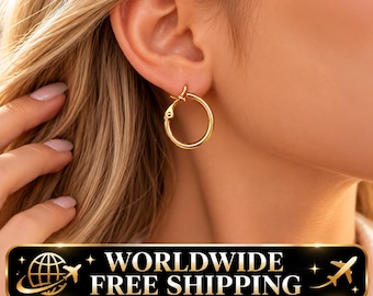 May include: A small, polished gold hoop earring with a hinged closure mechanism. The circular earring features a smooth, reflective metallic surface and is secured through the earlobe, showcasing a simple, continuous hoop design.
