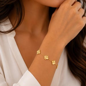 May include: A gold chain bracelet featuring multiple four-leaf clover charms. The bracelet is constructed with a delicate gold link chain connecting each clover motif, which has a textured surface finish and a small gold bead at the center.