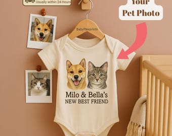 Könnte beinhalten: Ein cremefarbener Baby-Body mit Illustrationen eines Hundes und einer Katze sowie dem Text "Milo & Bella's NEW BEST FRIEND". Der Body hängt an einem Holzbügel. Zwei Haustierfotos sind darüber gepinnt.