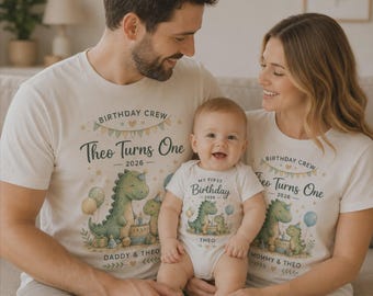 Może przedstawiać: Dwie koszulki w kolorze złamanej bieli oraz dziecięce body z grafiką zielonego dinozaura, balonami i napisem Birthday Crew, Theo Turns One, 2026. Koszulki mają napisy Daddy & Theo i Mommy & Theo, a na body widnieje napis My First Birthday.