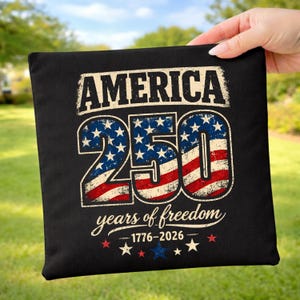 May include: Black square cushion featuring the text "AMERICA 250 years of freedom 1776-2026" in distressed white, red, and blue. The numbers "250" are designed with the American flag. Stars and stripes design.